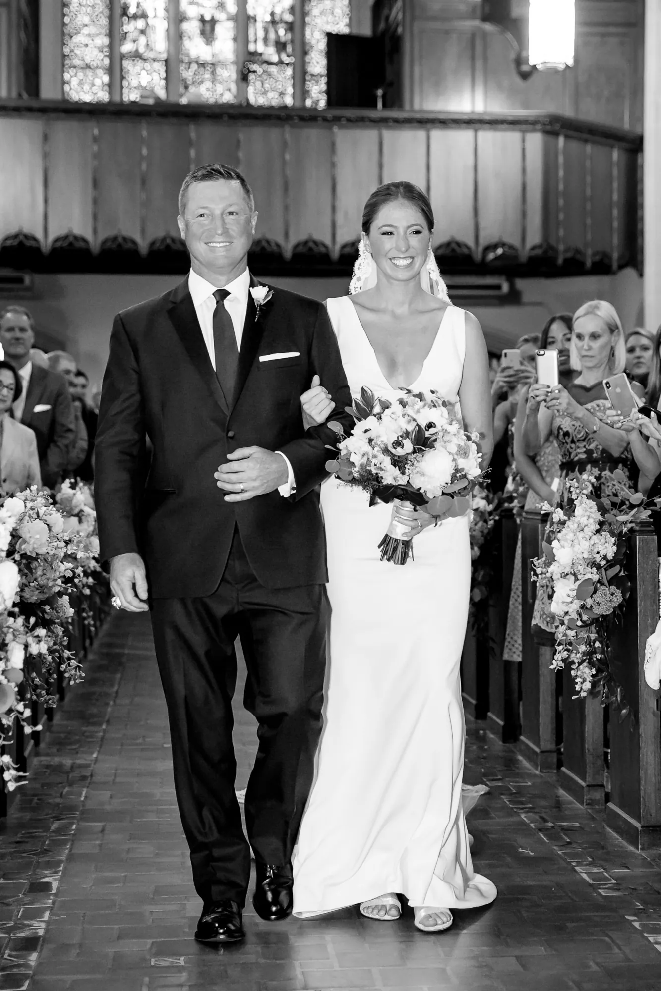 A gray-haired man walks the bride down the church aisle, in black and white