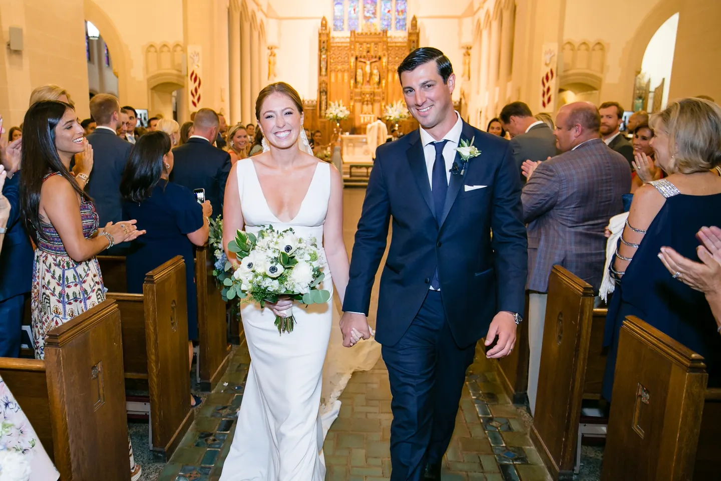 Anna and John walk back up the aisle past smiling guests in the wooden pews