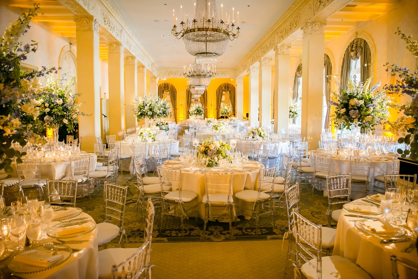 The ballroom glows gold with chandeliers, arched windows, and round tables set for dinner