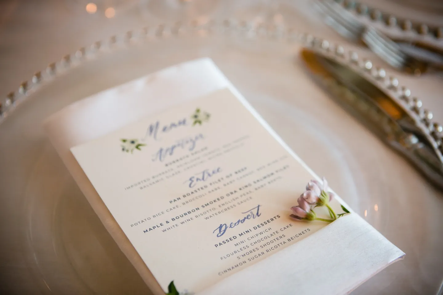 A printed menu rests on a gold-rimmed plate at a candlelit place setting