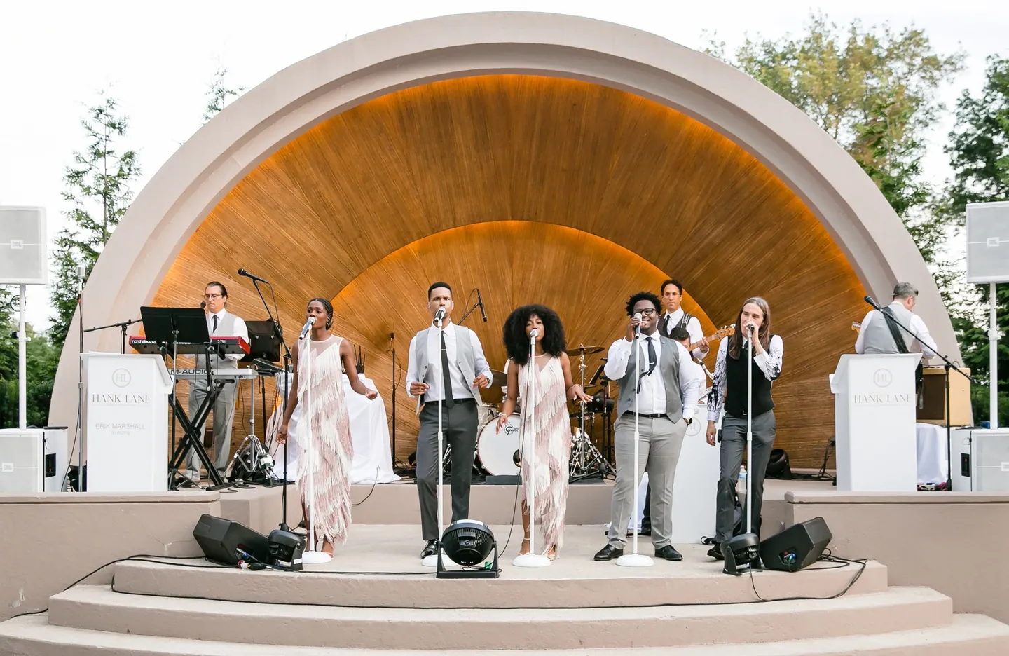 A live band performs under the curved wooden band shell at dusk