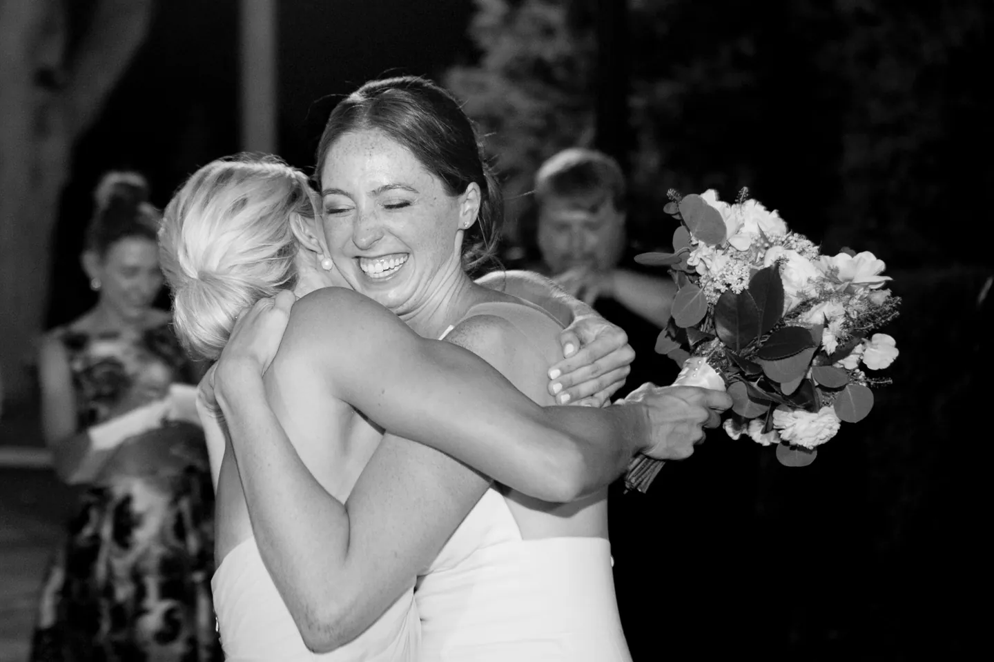 The bride hugs a friend tightly on the dance floor, in black and white