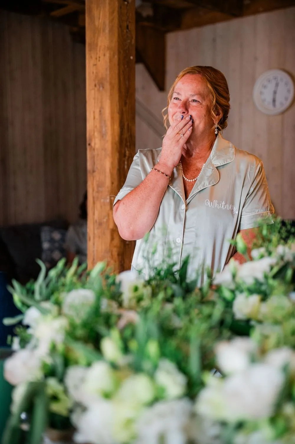 A woman in a mint satin shirt covers her mouth, moved, behind a blur of white flowers