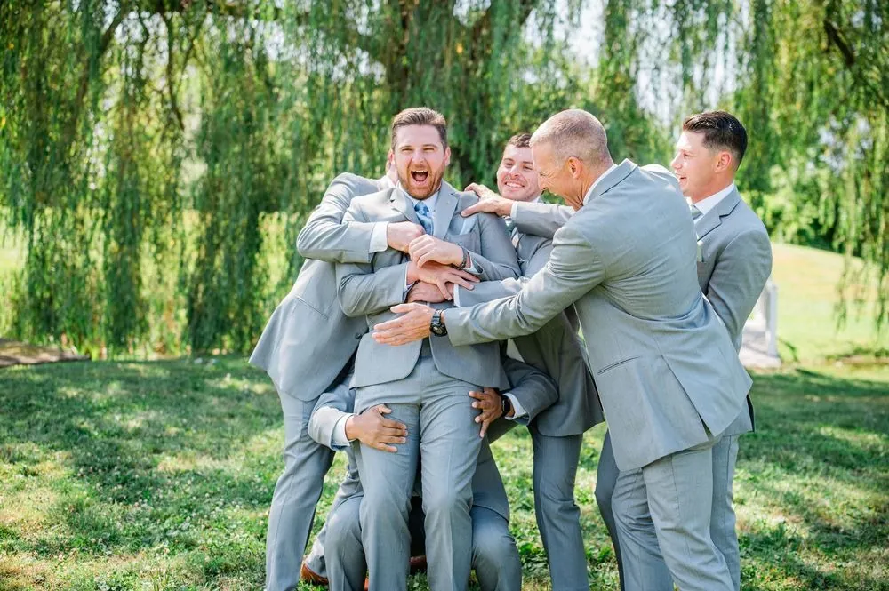 Groomsmen pile into a group hug with the groom under the willows