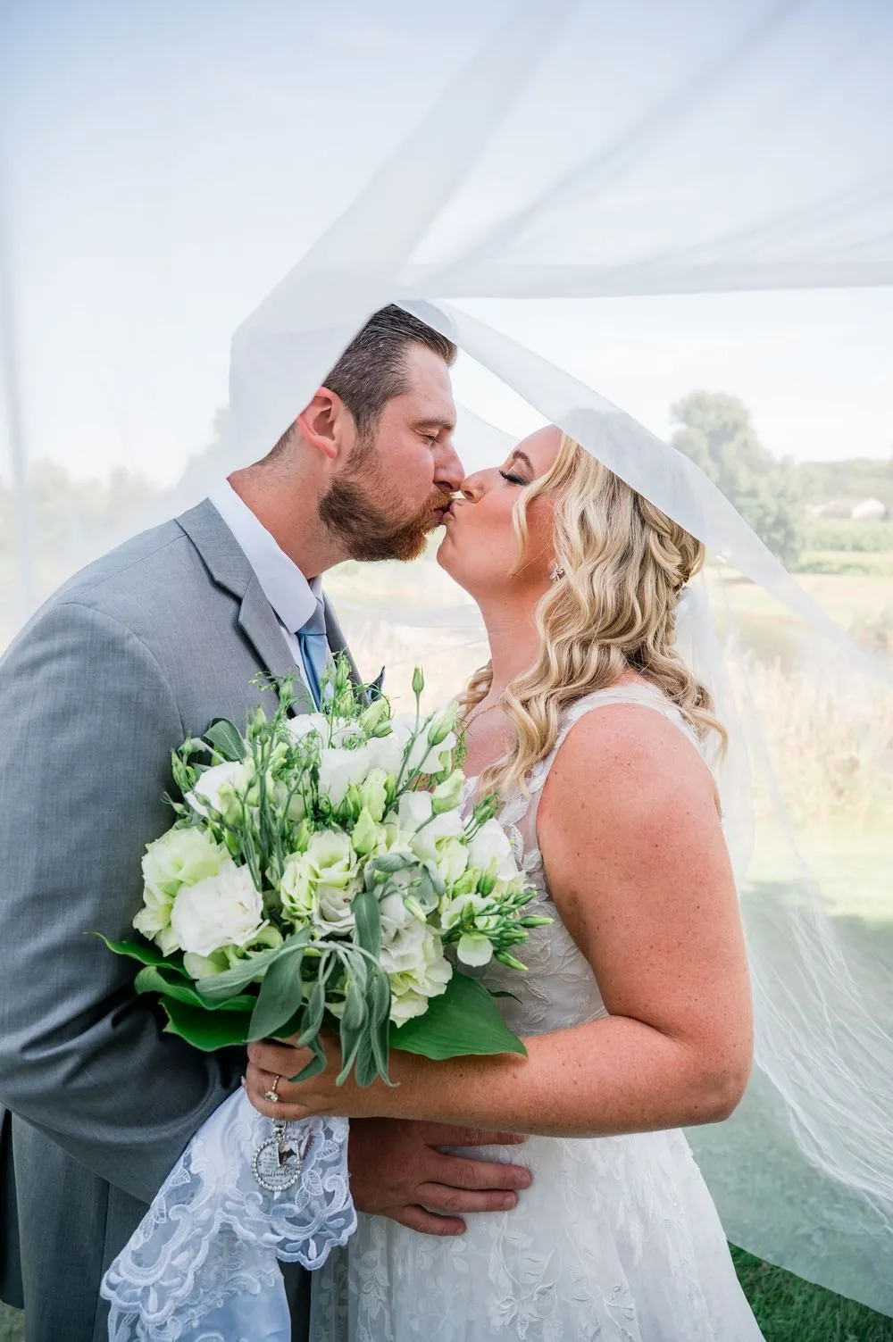 Arianne and Michael kiss with her white rose bouquet between them
