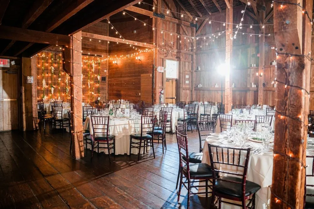 The barn reception set with dark chairs and string lights strung along the loft