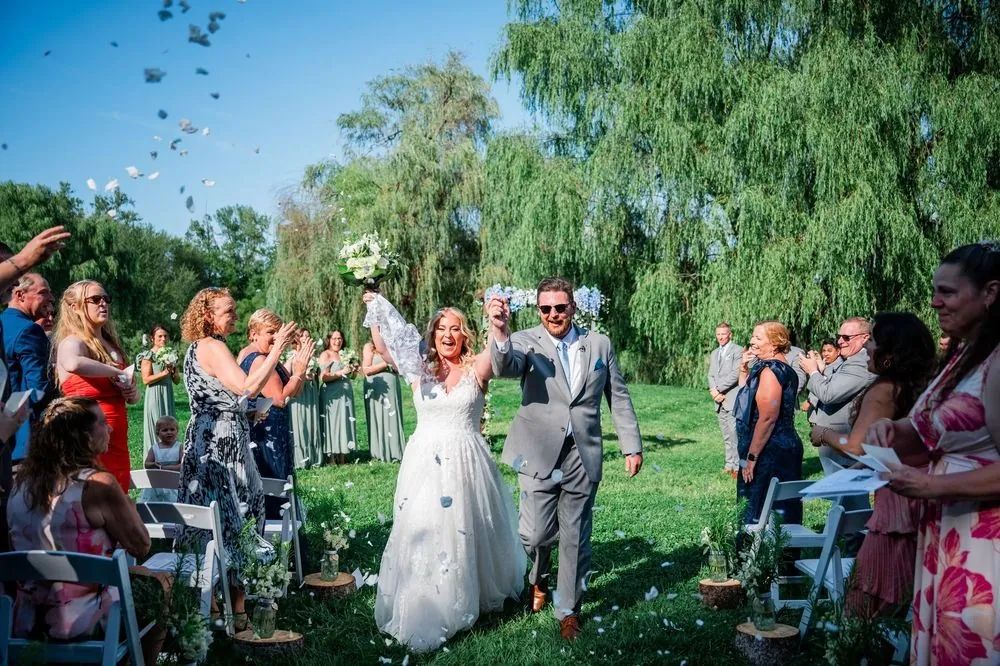 Arianne raises her bouquet and Michael pumps a fist as petals fly on the recessional