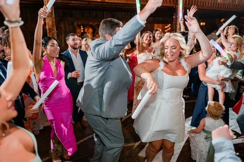The bride in a short white dress dances with guests waving foam glow sticks