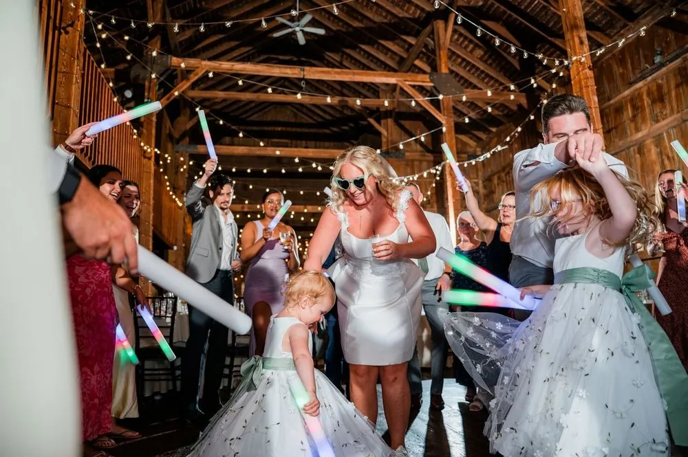 Guests crowd the barn dance floor with glow sticks raised under the lights