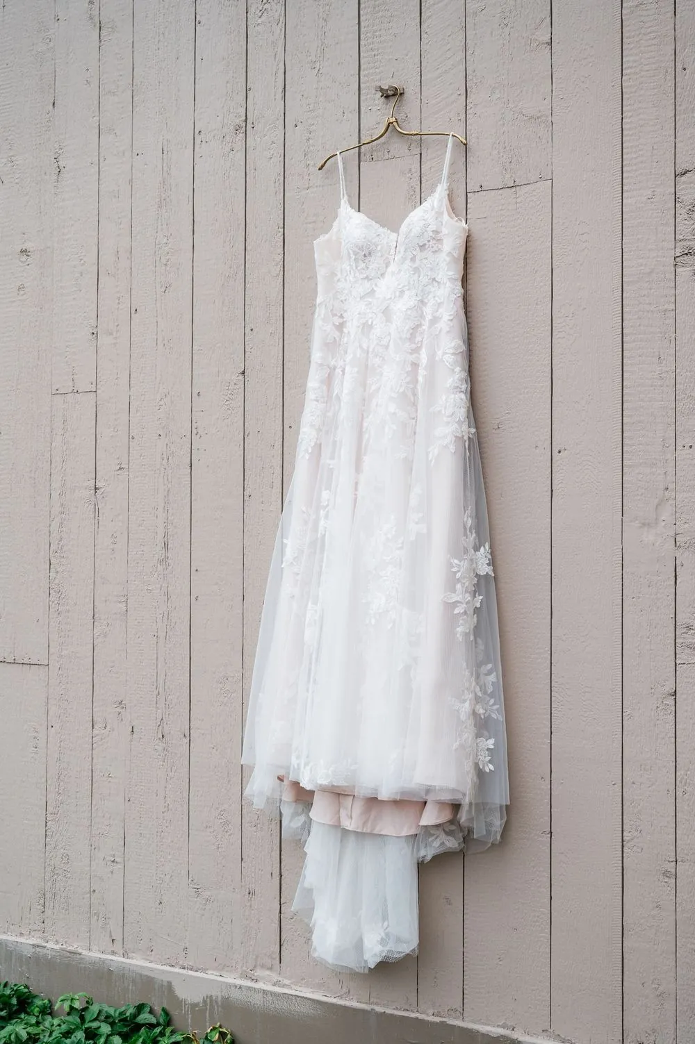 Lace wedding gown hanging against a pale wood-paneled wall