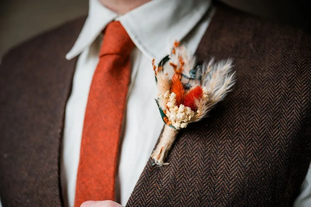 Close view of a rust-orange tie and dried-flower boutonniere pinned to brown tweed