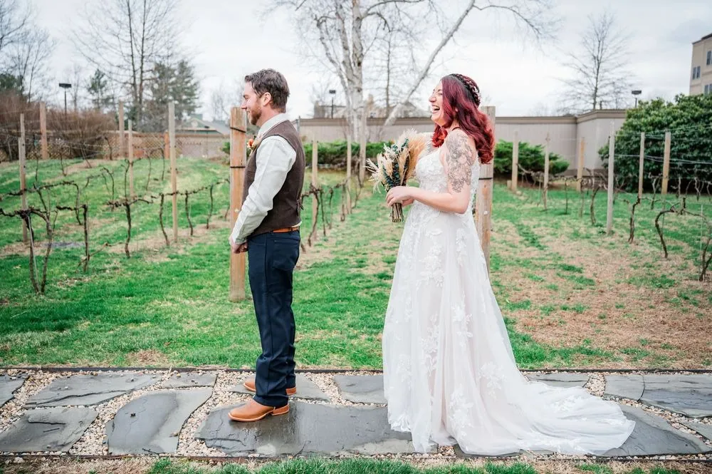 Ashley and Brian face each other on a stone path during their first look beside the vines