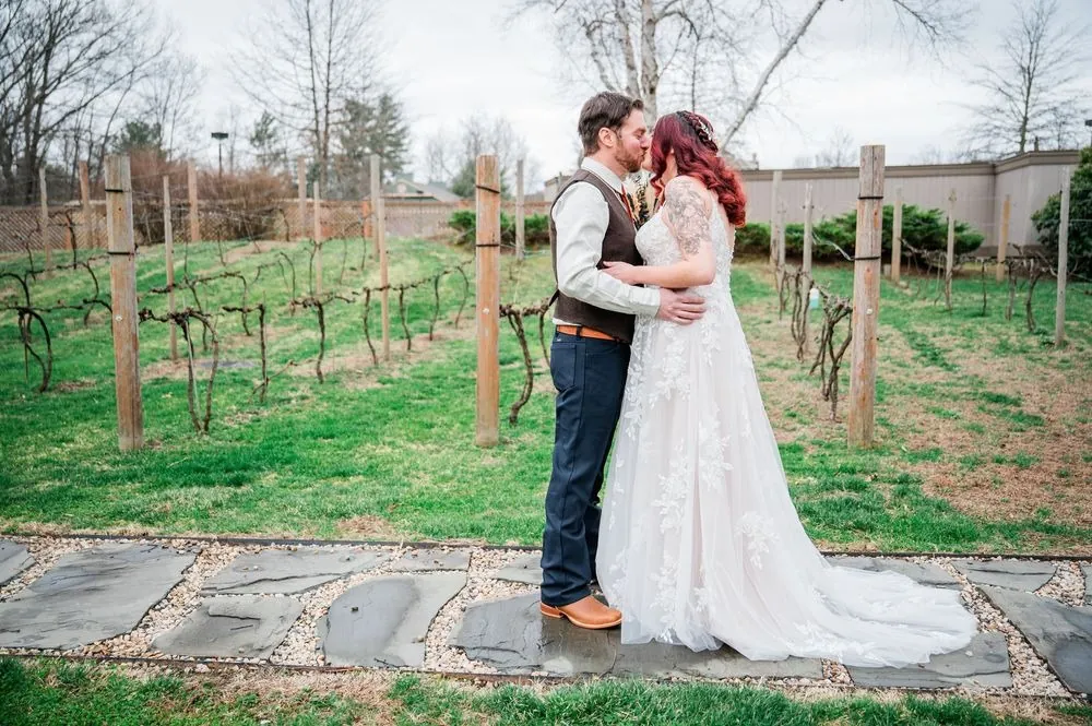 Ashley and Brian hold each other close among bare grapevines under a grey spring sky