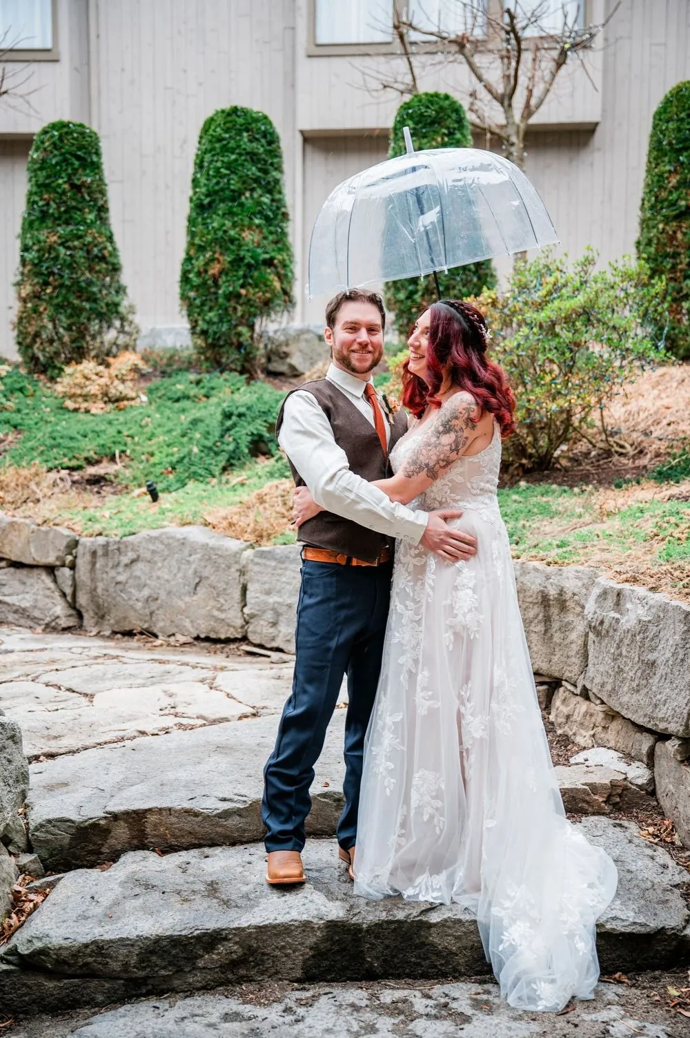 Ashley and Brian laugh under a clear bubble umbrella on the courtyard's stone steps