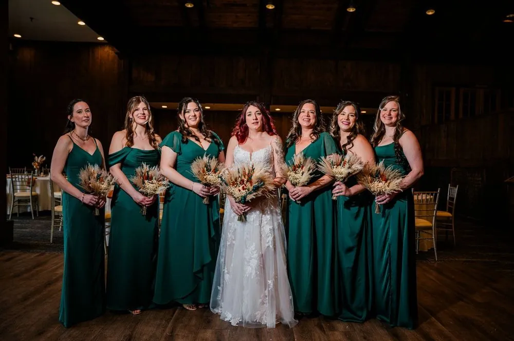 The bride with her bridesmaids in forest green gowns inside the wood-beamed reception hall