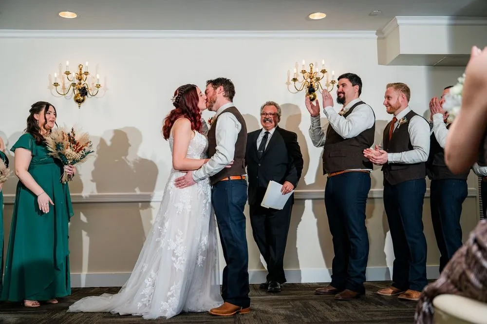 Ashley and Brian share their first kiss as groomsmen clap and the officiant smiles