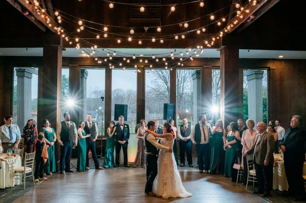 Ashley and Brian's first dance under string lights, guests circled by tall windows at dusk