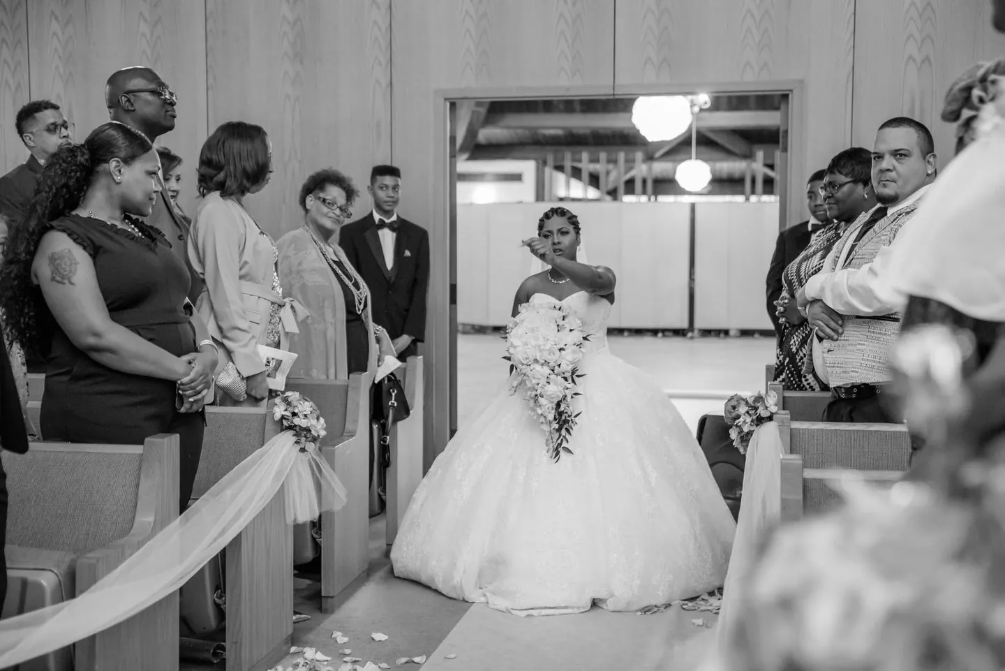 The bride enters the church singing, one hand raised toward the altar, in black and white