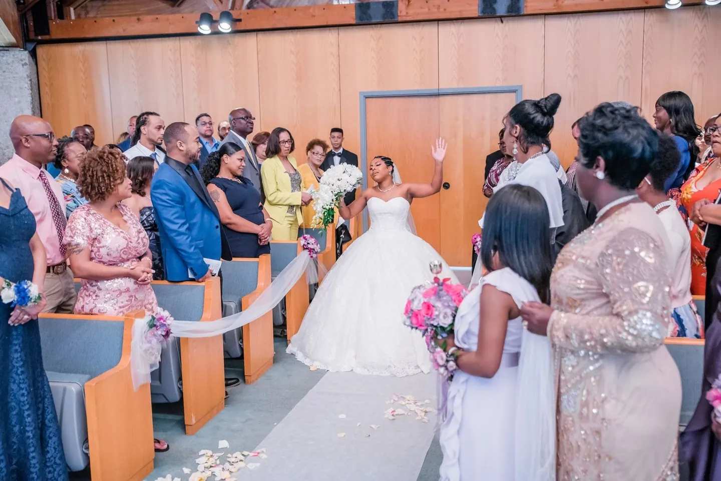 Guests stand and turn as the bride walks down the aisle in her ballgown