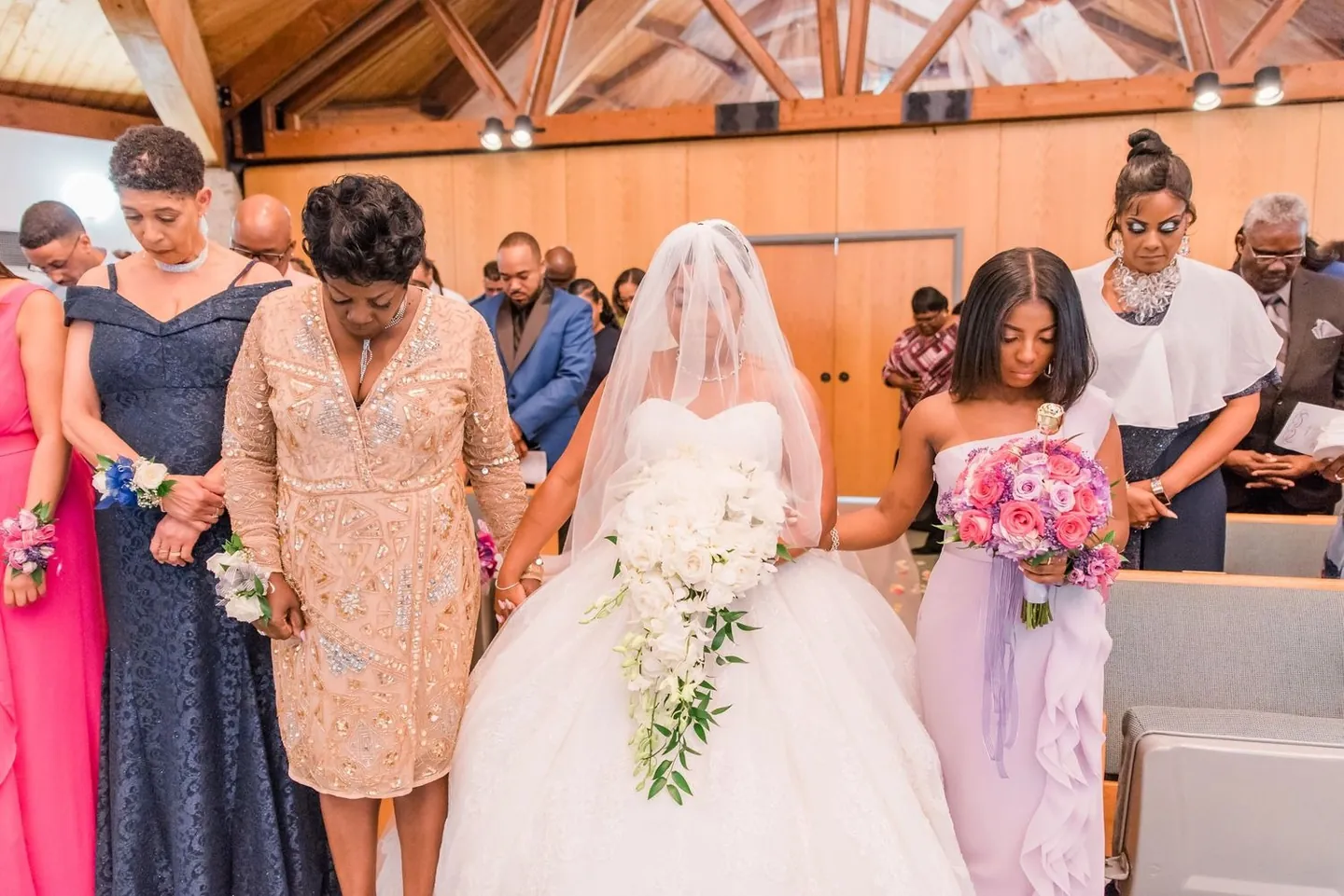 Family members bow their heads in prayer around the bride in the aisle