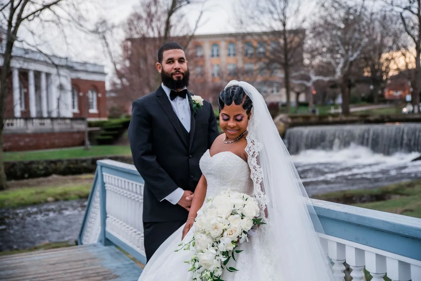 Ashley and Darren stand on a white footbridge above a rushing spillway