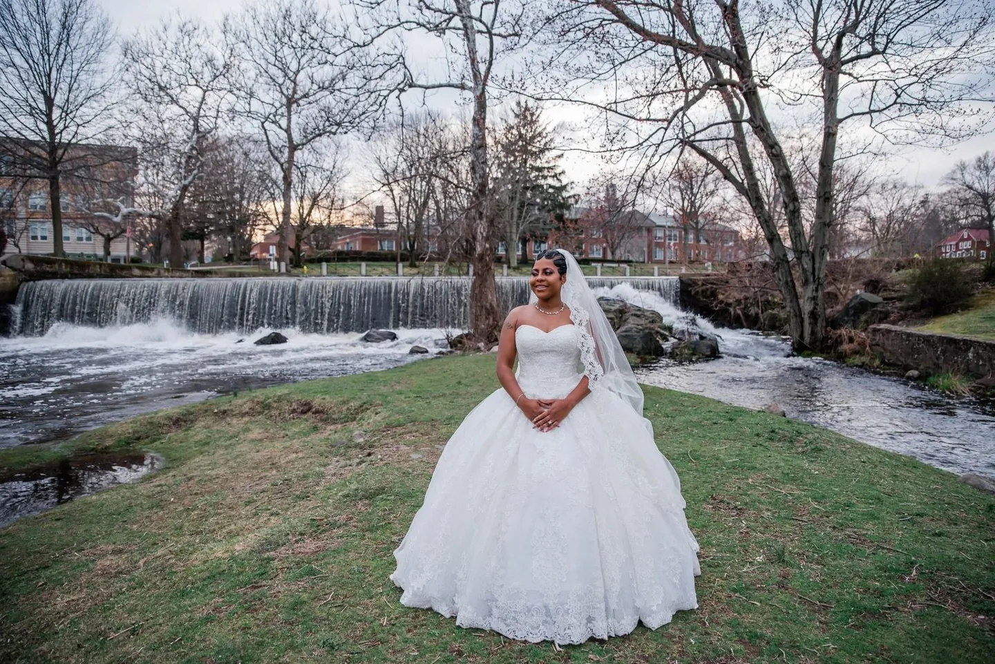 The bride stands alone on a grassy point with a waterfall rushing behind her