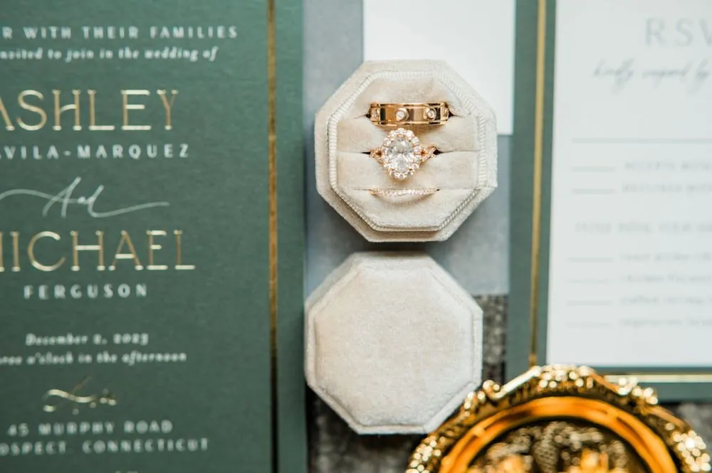 Wedding rings in a cream velvet box on a deep green and gold invitation