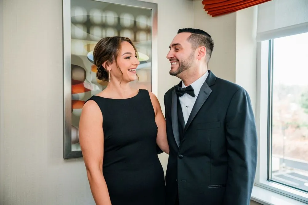 The groom shares a laugh with a woman in black by the window before the ceremony