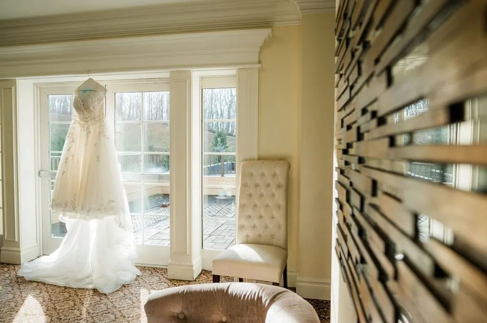 The wedding gown hangs in a sunlit room by tall French doors
