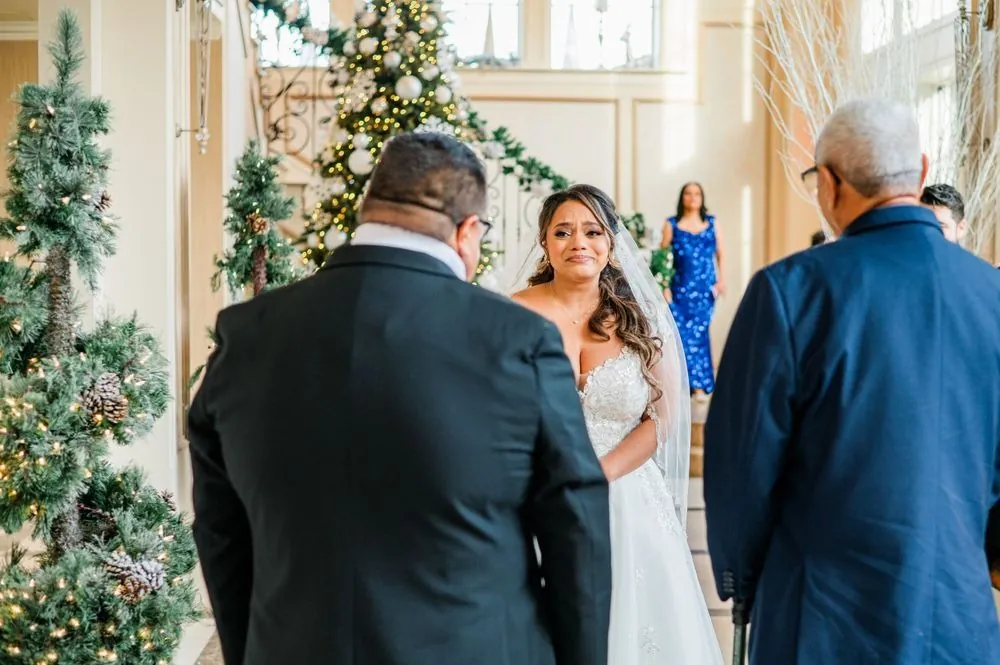 The bride's father and grandfather watch her come down the garland staircase