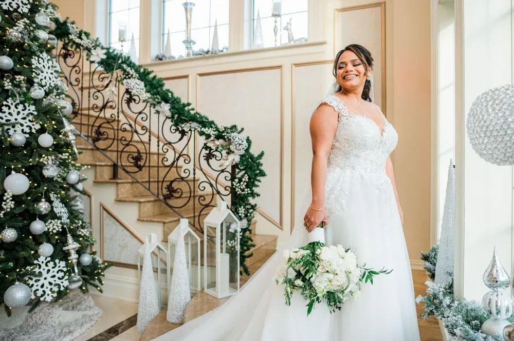 The bride stands at the foot of a staircase wrapped in holiday garland
