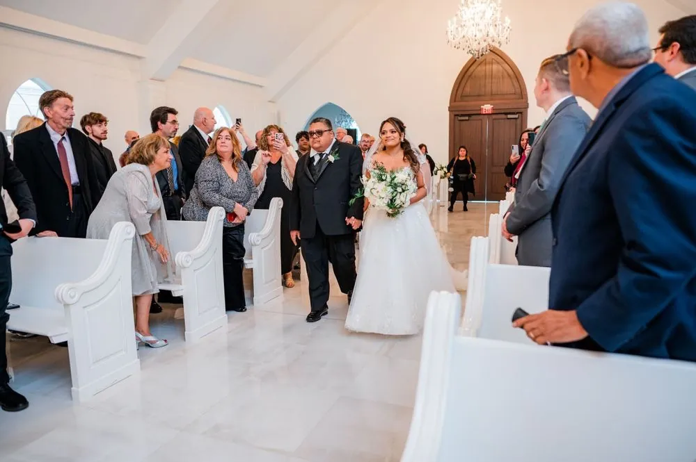 The bride walks down the chapel aisle as guests turn to watch