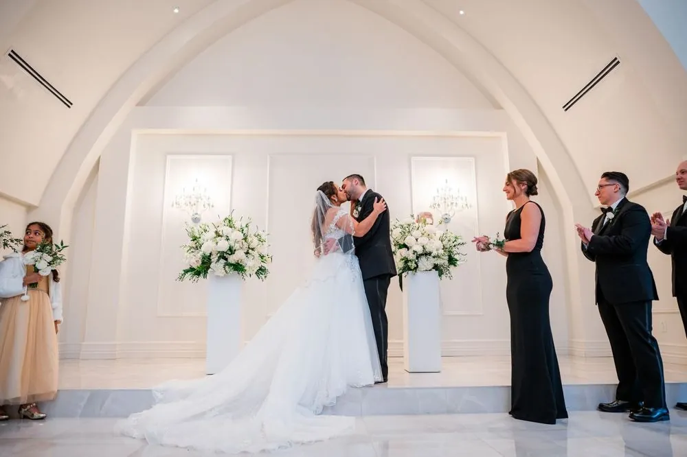 Ashley and Michael kiss in the white arched chapel between tall white flowers