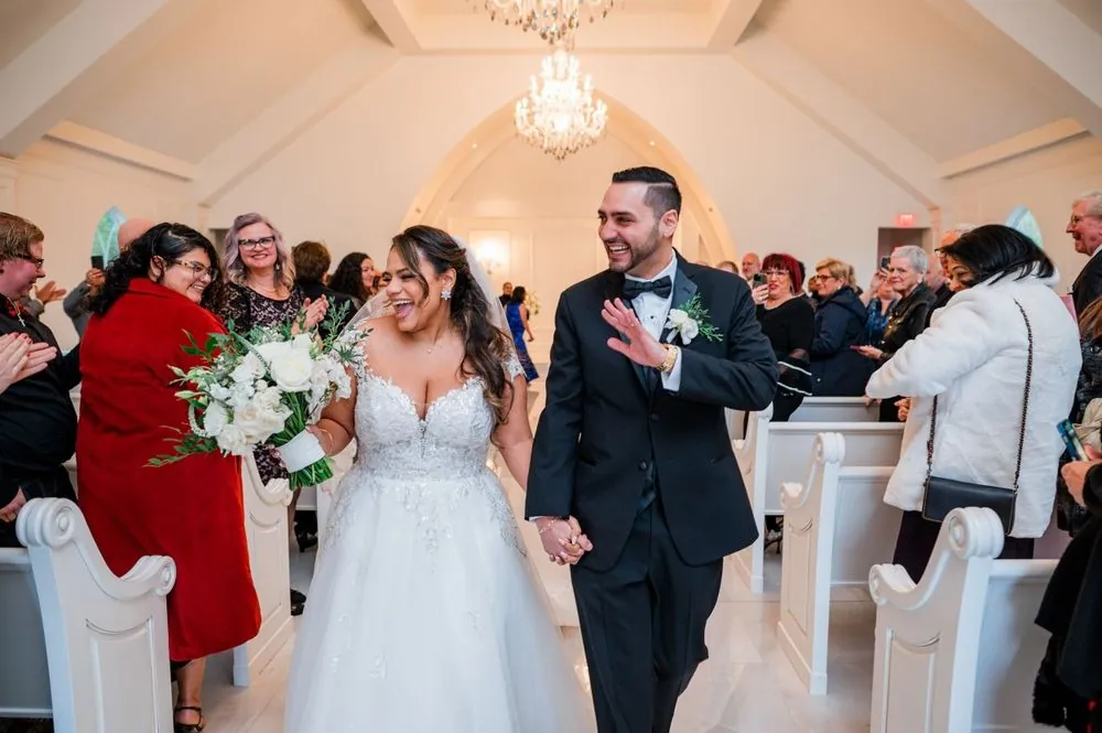 Guests cheer as the newlyweds walk back up the aisle between white pews