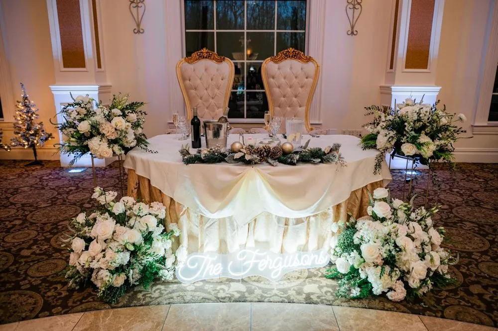 A sweetheart table with white flowers and uplighting in the ballroom
