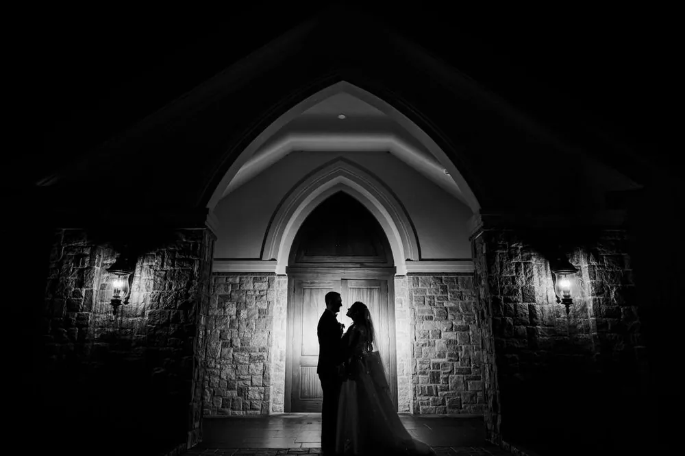 Black and white silhouette of the couple in the lit chapel doorway at night