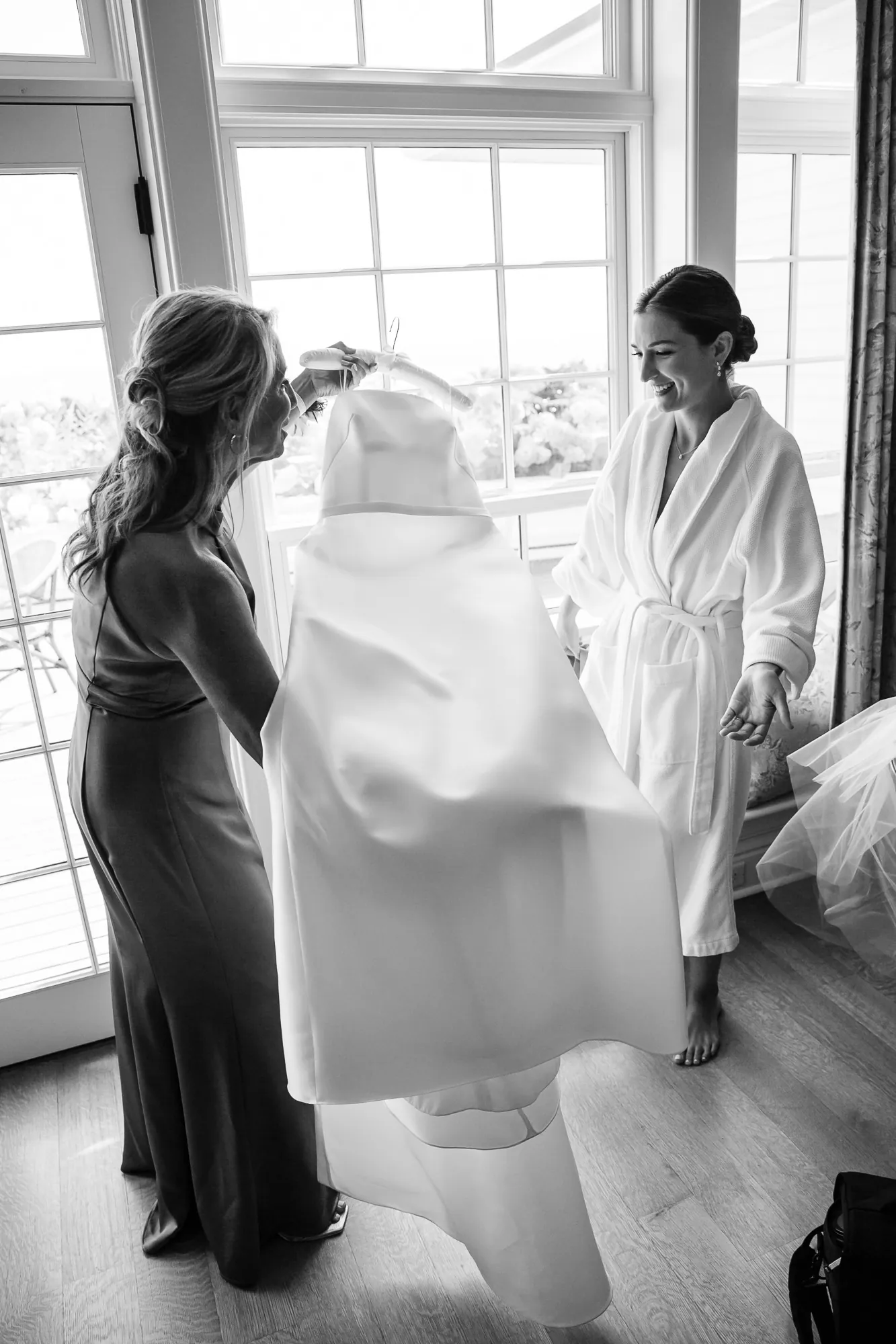Black and white frame of the bride stepping into her gown beside a tall bright window
