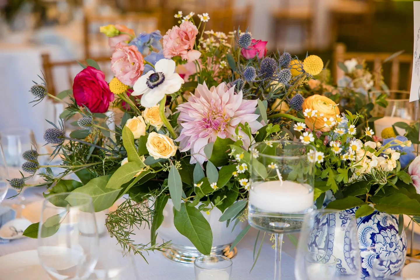 A low centerpiece of dahlias, anemones and roses in a blue and white porcelain vase