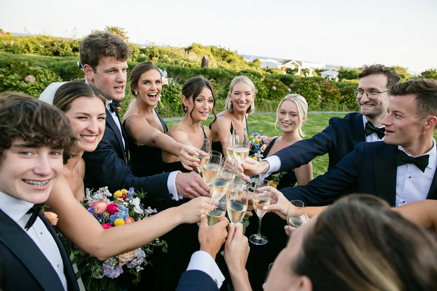 Friends raise champagne flutes toward the couple in a tight circle on the lawn
