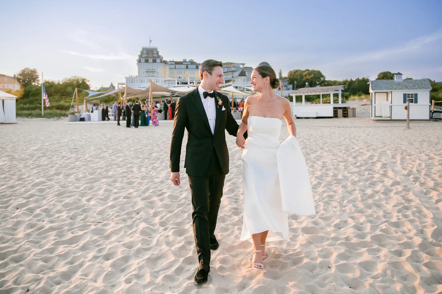 Avery and Dan stroll across the sand with the Ocean House roofline rising behind them