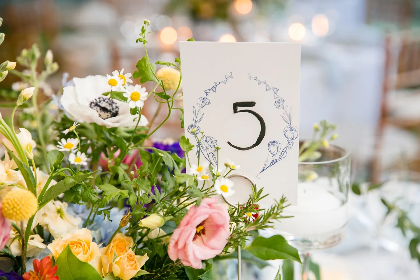 Table number 5 tucked into a loose arrangement of anemones and roses under warm tent light