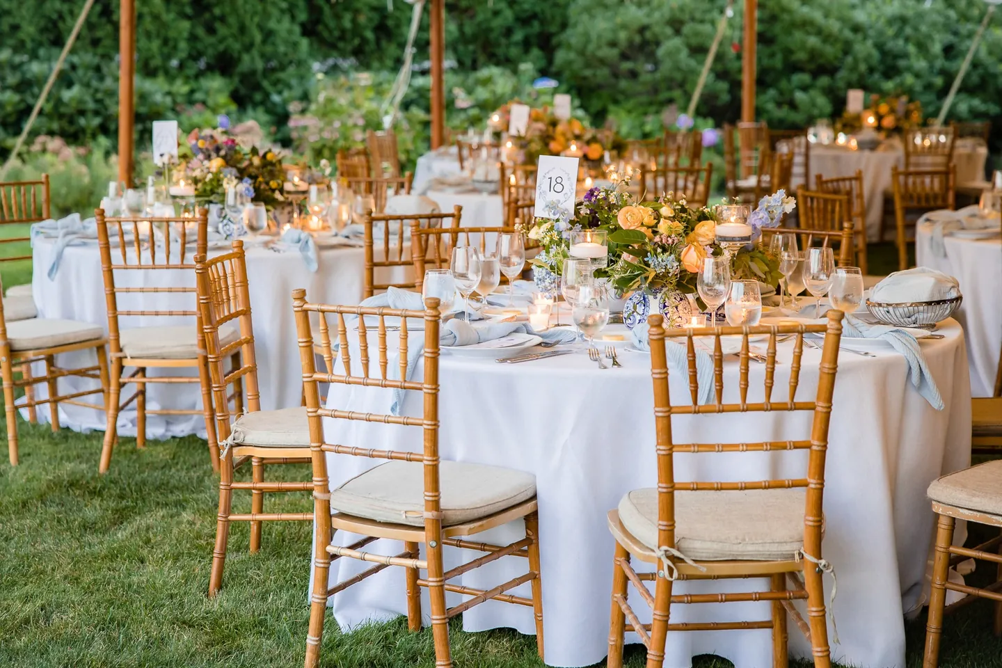 Round tables with gold chairs and bright centerpieces set under the reception tent