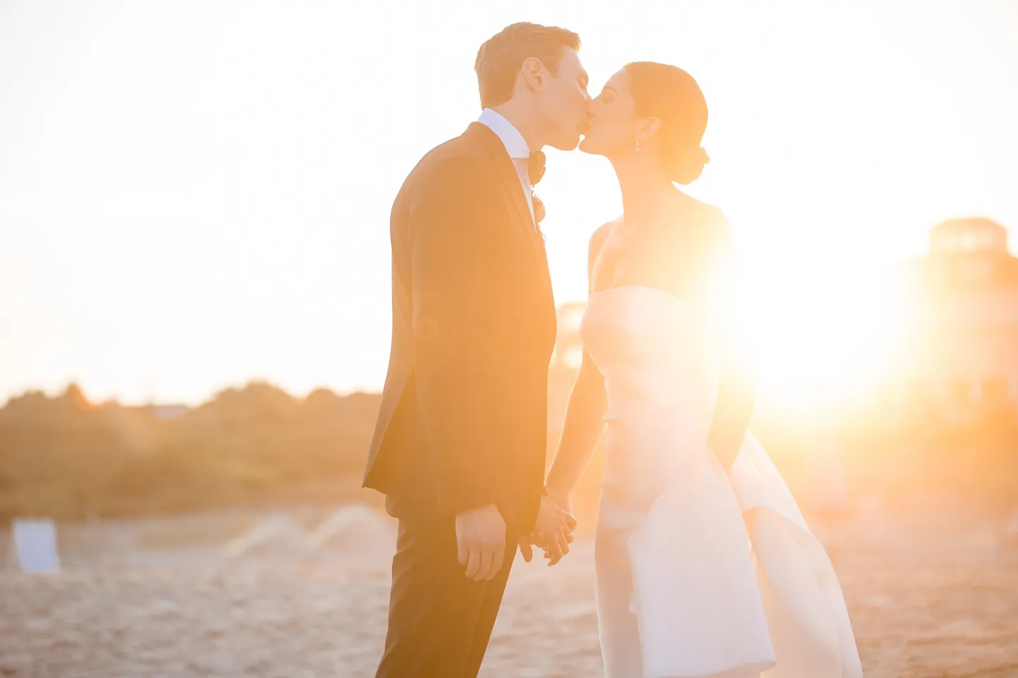 Avery and Dan kiss on the beach as the setting sun flares warm gold behind them