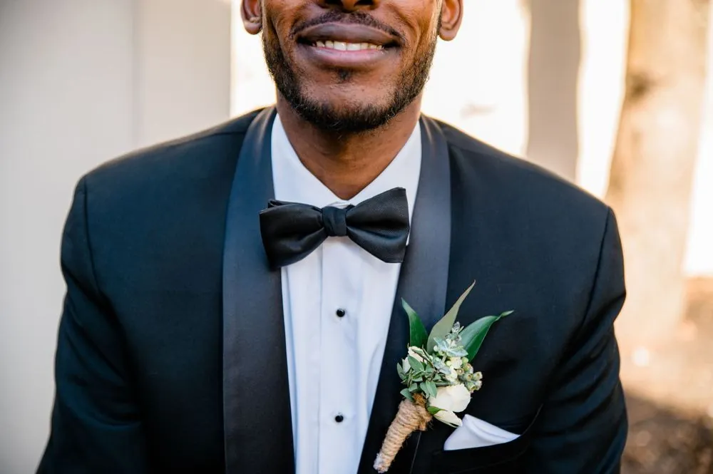 Close view of the groom's smile, black bow tie and greenery boutonniere