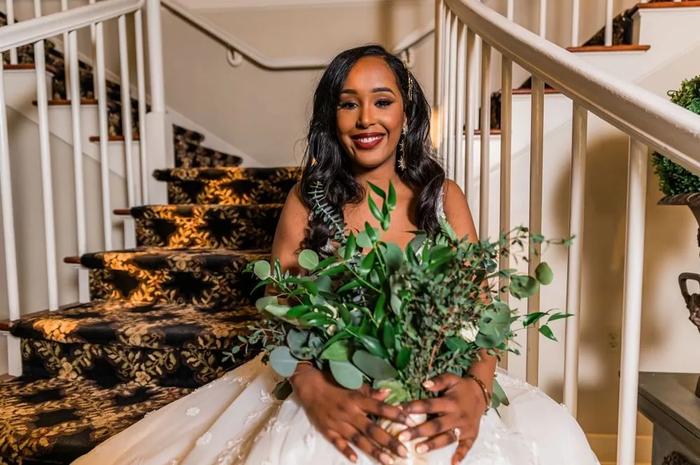 The bride smiles on the carpeted staircase with a large green bouquet