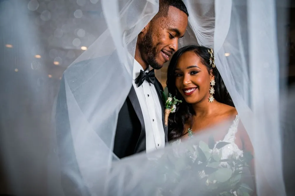 Ayan and Guleid smile close together beneath her sheer veil, ballroom lights glowing behind