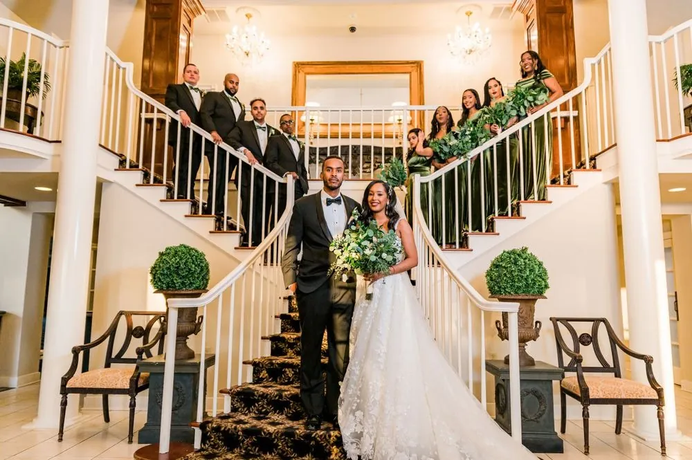 The wedding party fills the white double staircase around the couple