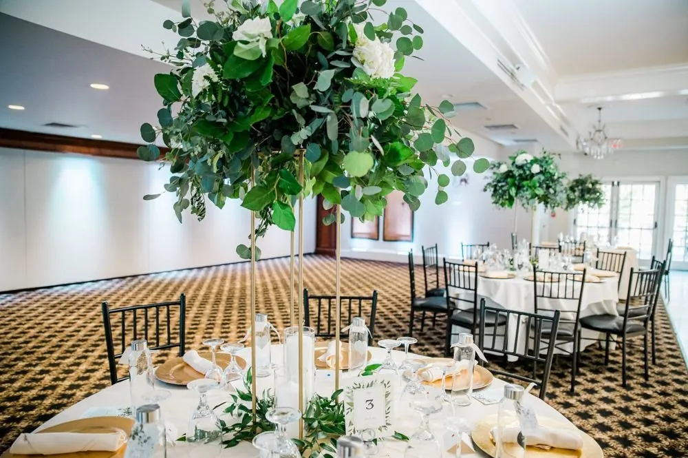 A tall greenery centerpiece rises over round tables in the reception room