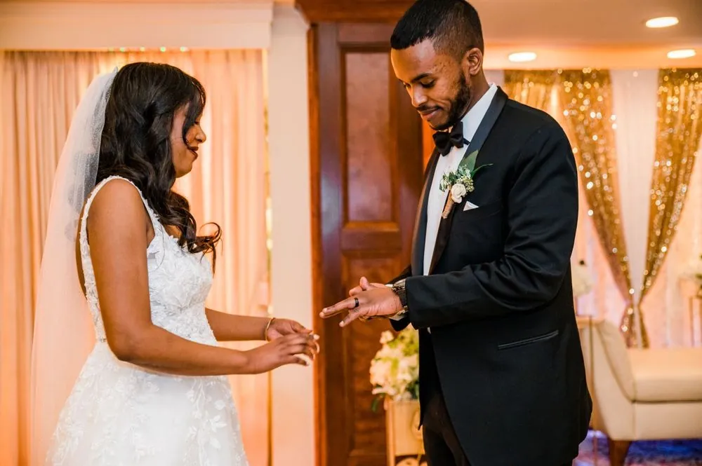 The bride and groom exchange rings in front of gold sequin drapes