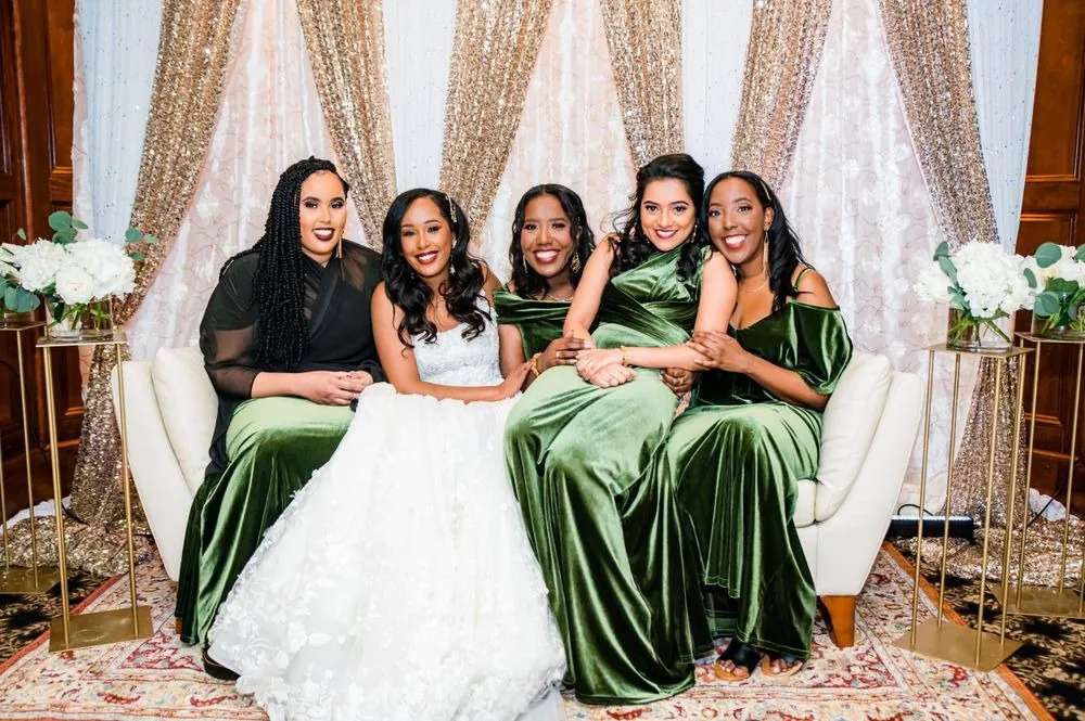 The bride sits on the cream sofa surrounded by bridesmaids in olive velvet